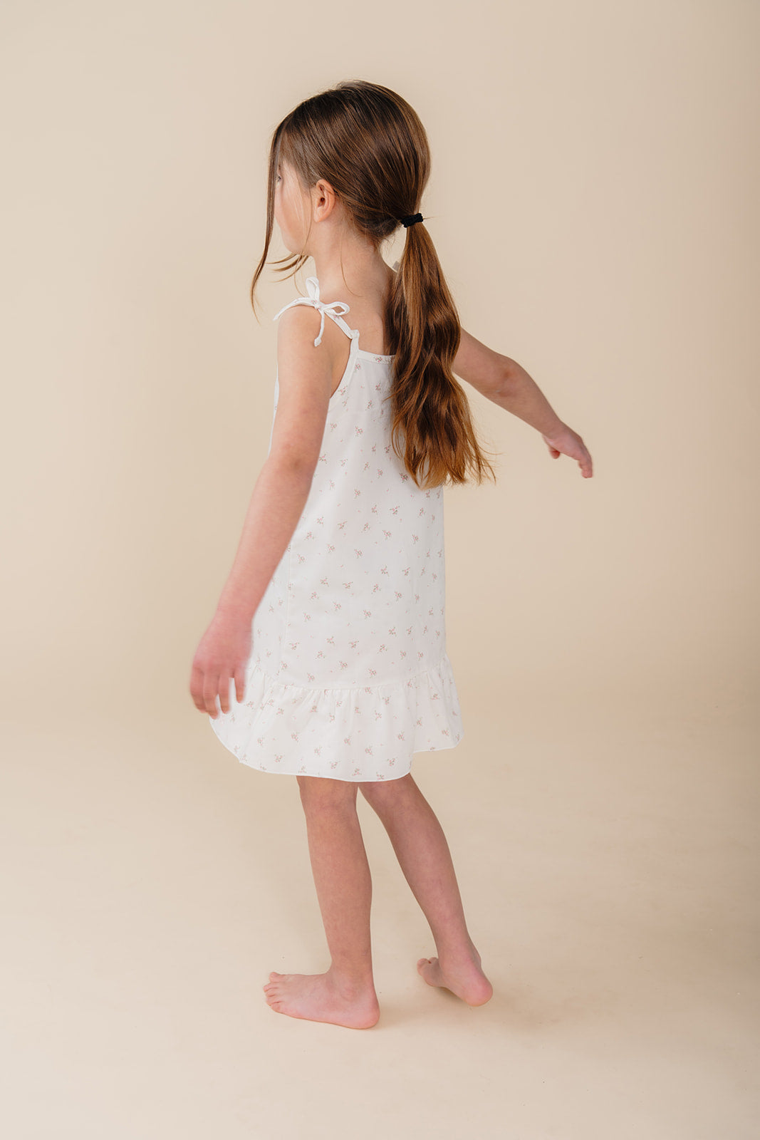 Meisje in witte katoenen pyjama-jurk met bloemenprint uit de Cozy Dawn collectie van Atelier Bonheur, duurzame nachtkleding voor kinderen.

