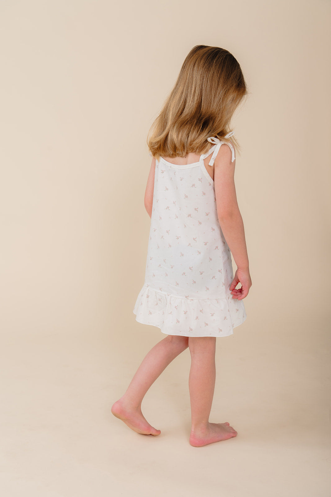 Meisje in witte katoenen pyjama-jurk met bloemenprint uit de Cozy Dawn collectie van Atelier Bonheur, duurzame nachtkleding voor kinderen.