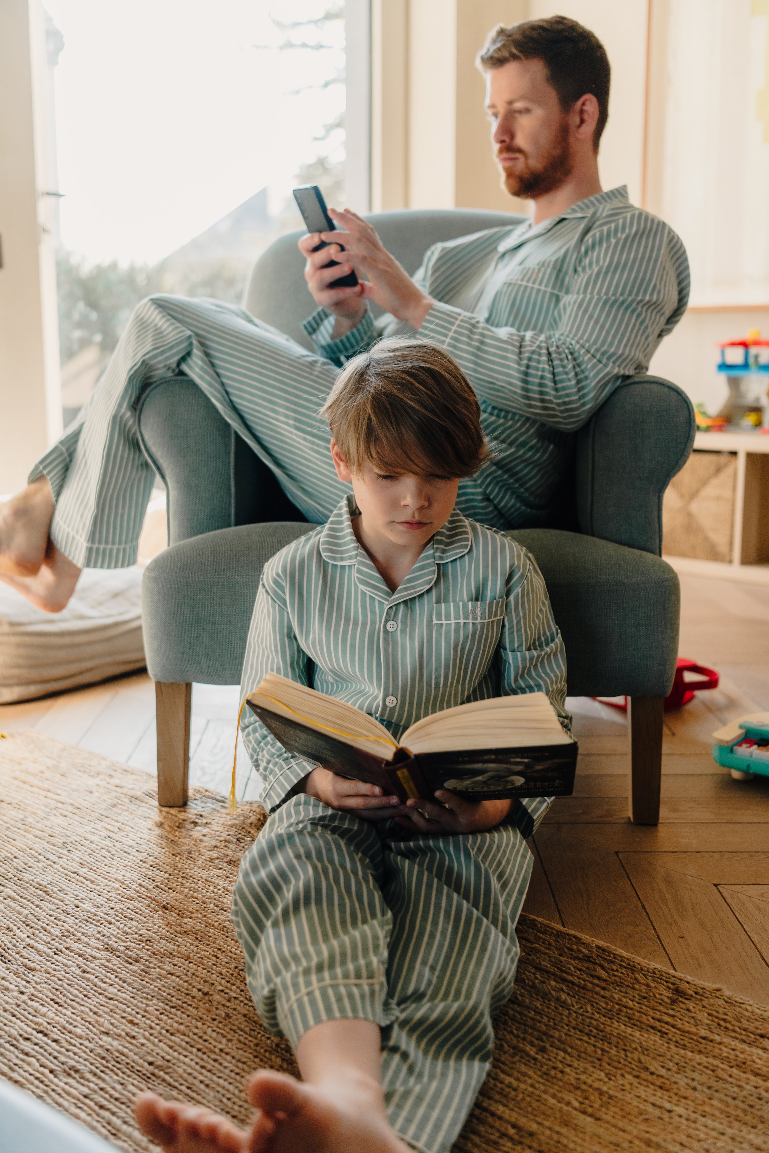 Gezin geniet van een rustig moment in de woonkamer in bijpassende pyjama’s uit de Striped Dreams collectie van Atelier Bonheur. Gemaakt van zacht katoen, ontworpen voor comfort en verbondenheid.

