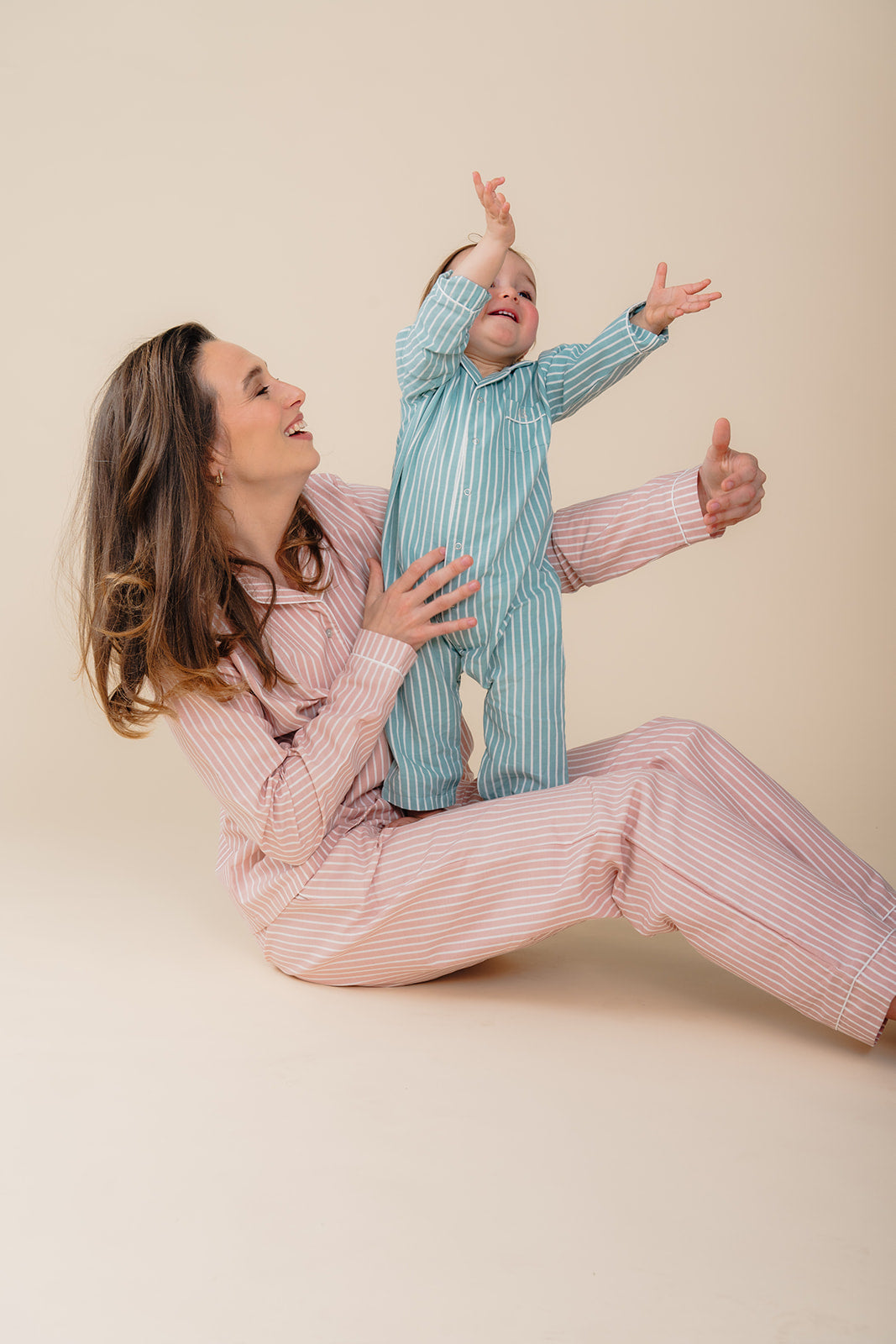 Moeder en baby spelen samen in zachte katoenen pyjama’s uit de Striped Dreams collectie van Atelier Bonheur, met comfortabele streepjes en warme momenten thuis.

