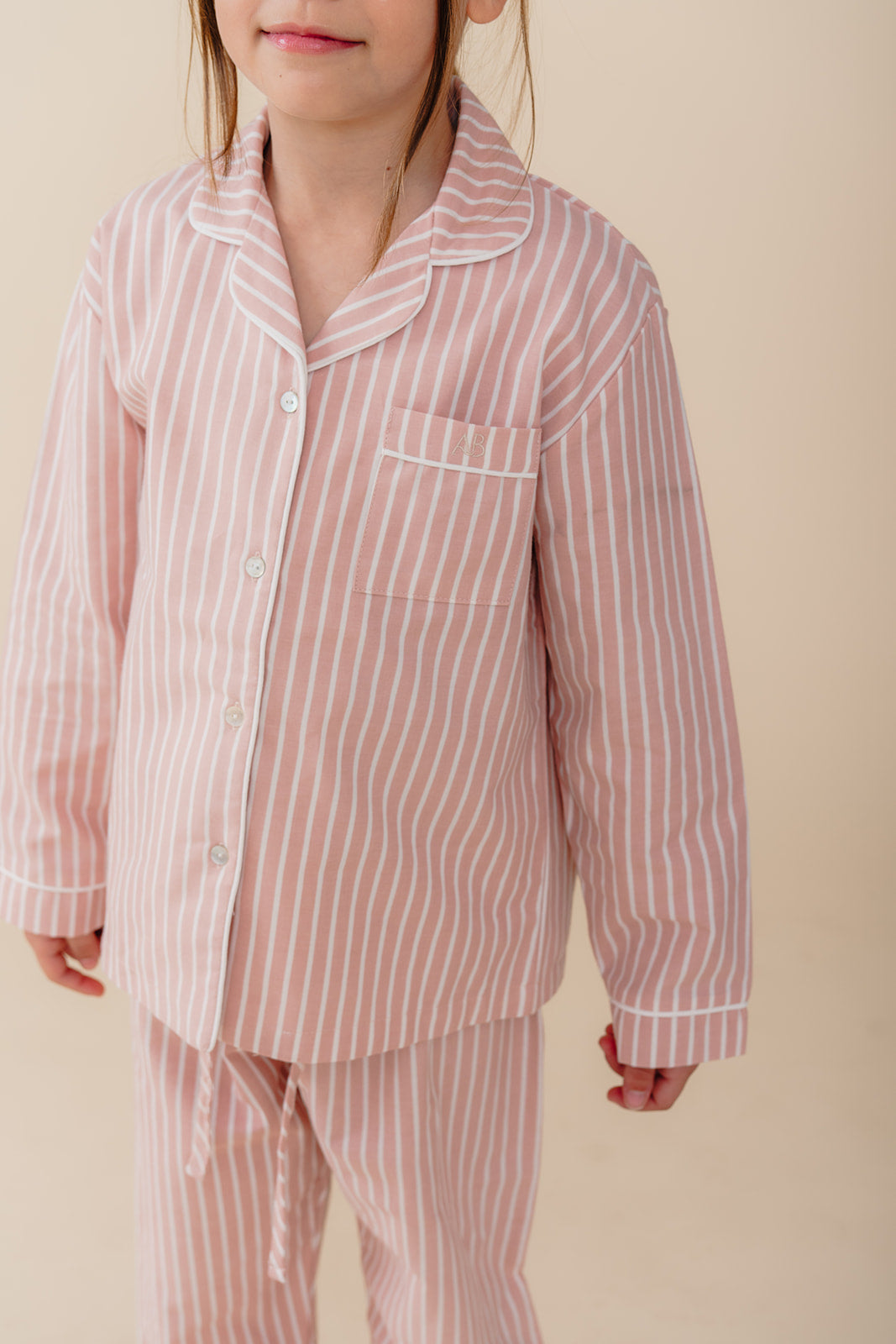 Meisje draagt een roze gestreepte katoenen pyjama uit de Striped Dreams collectie van Atelier Bonheur. Comfortabele en stijlvolle nachtkleding voor kinderen.

