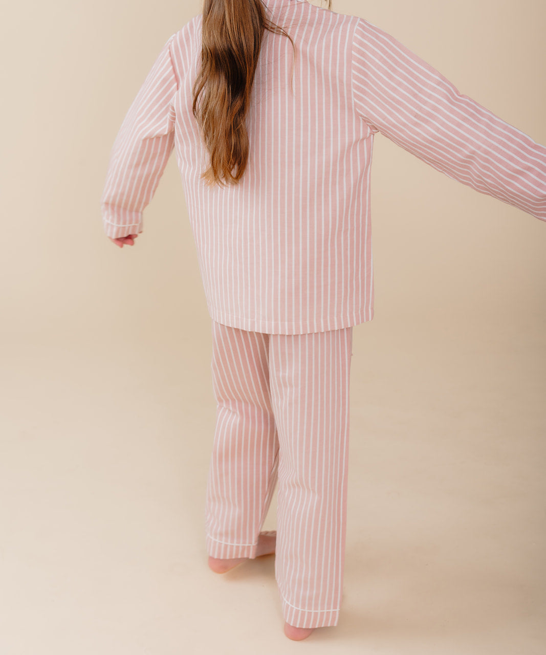 Meisje draagt een roze gestreepte katoenen pyjama uit de Striped Dreams collectie van Atelier Bonheur. Comfortabele en stijlvolle nachtkleding voor kinderen.

