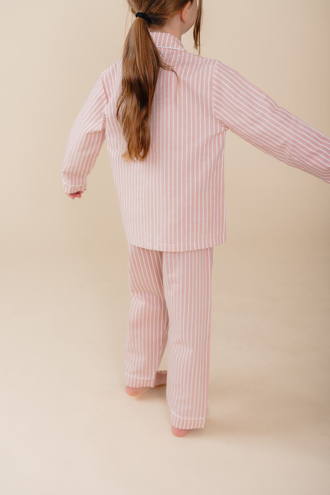 Meisje draagt een roze gestreepte katoenen pyjama uit de Striped Dreams collectie van Atelier Bonheur. Comfortabele en stijlvolle nachtkleding voor kinderen.

