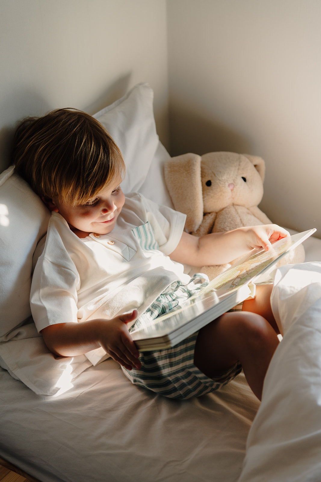 Jongen leest in bed in pyjama van atelier bonheur met tshirt en streepjes short en zachte atelier bonheur boncoeur knuffelbeer.